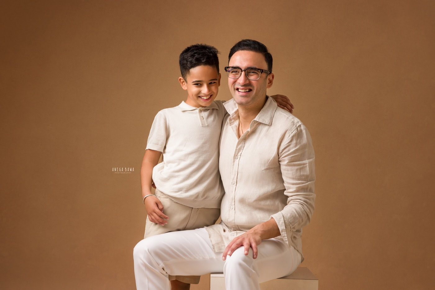 Warm-toned portrait of a happy father and son smiling, dressed in beige, professional studio photography, Anega Bawa Photography, family photography, authentic candid moment, close-up.