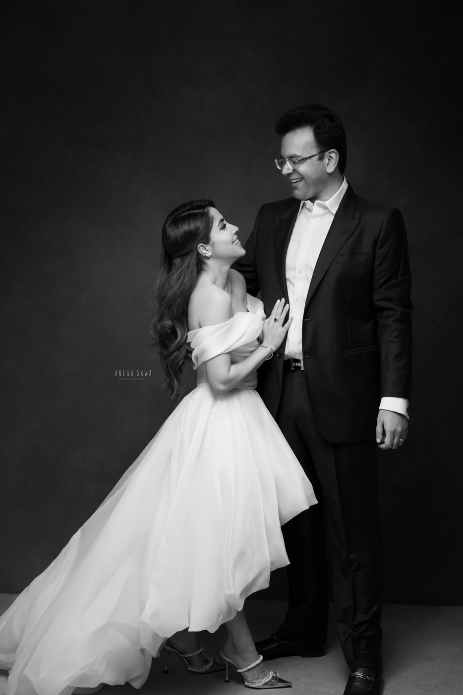 Husband and wife in a loving pose against a black backdrop in a black-and-white family photography session by Anega Bawa in Delhi, Gurgaon. The classic tones beautifully capture their affection and connection.