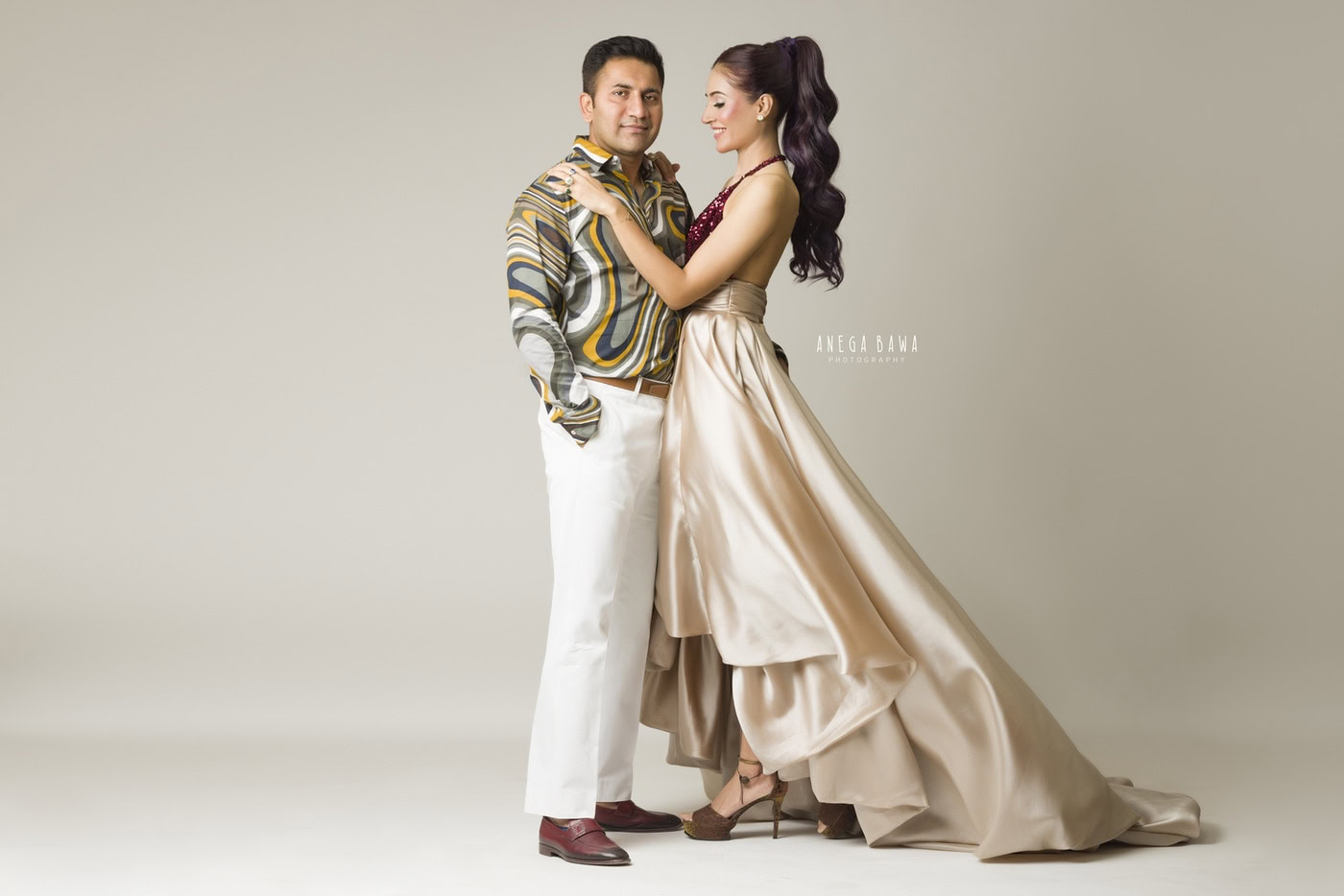 Elegant couple portrait in stylish clothing, professional photography by Anega Bawa, showcasing fashion and portrait photography in a minimalistic studio setting.