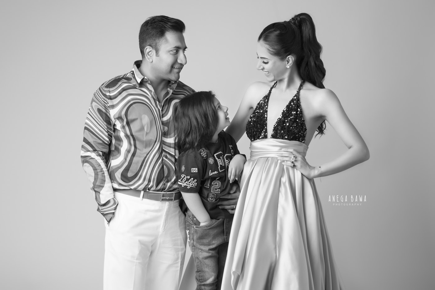 Mom, Dad, and their son in a retro look against a black-and-white backdrop, showcasing a stylish family moment captured by Anega Bawa in Delhi, Gurgaon. This photograph highlights their fashionable attire and the timeless charm of family photography.