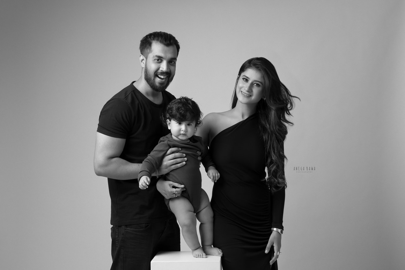 Happy family portrait with parents and toddler in black and white, professional photography by Anega Bawa focusing on family moments, kids, and portraits.