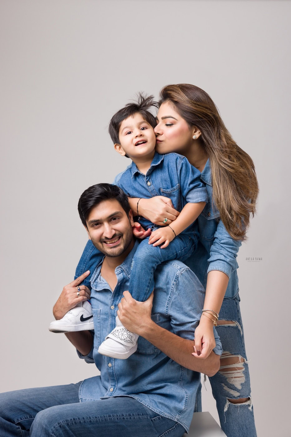 Mom, dad, and their son all wearing denims, posing together against a grey backdrop, captured during a family photography session by Anega Bawa in Delhi, Gurgaon. Their coordinated outfits and happy expressions showcase the strong bond they share as a family.