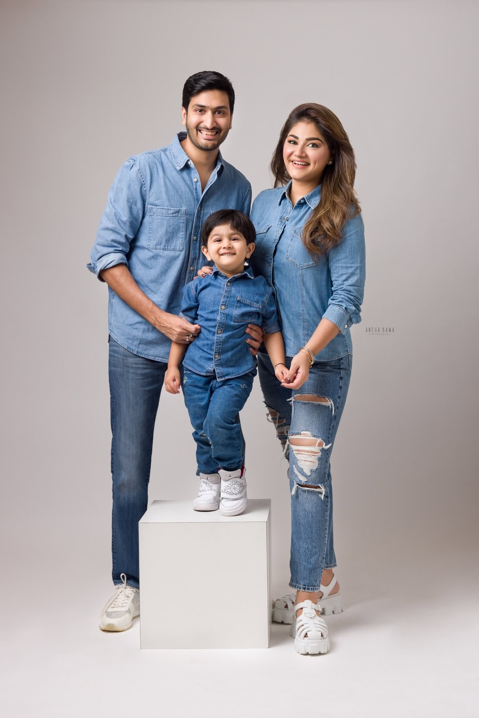 Happy family portrait in denim attire, capturing joyful moments with a young boy standing on a white platform against a neutral background.