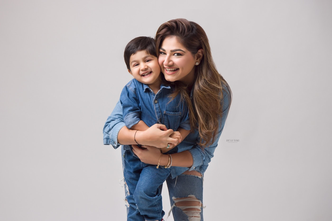 Happy mother and son cuddling, smiling, in casual denim, joyful family portrait, positive emotions, studio photography, Anega Bawa Photography, authentic moment, heartwarming scene.