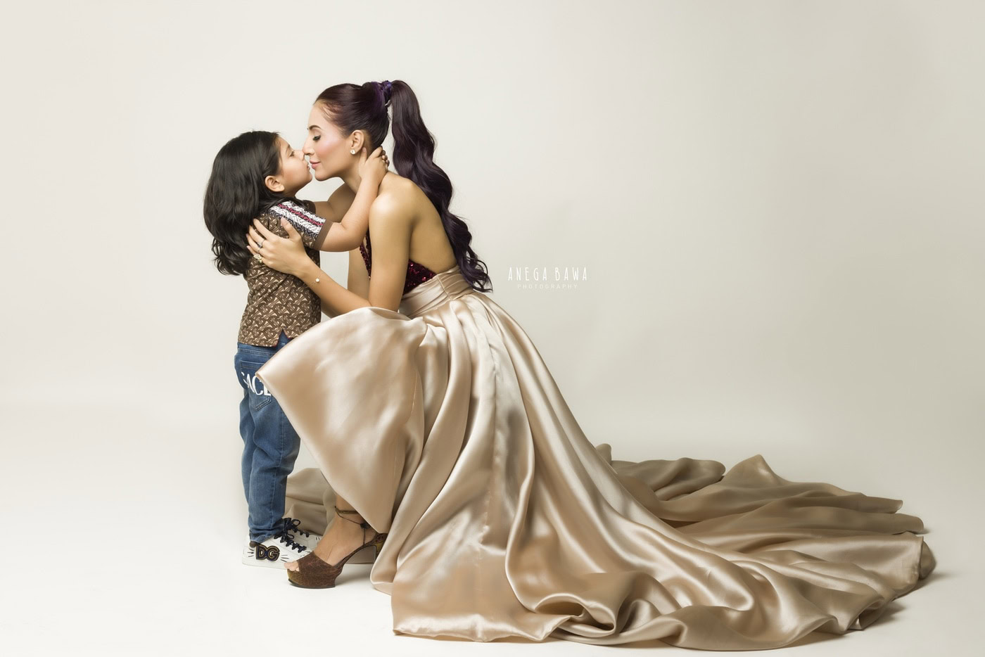 Mom and son sharing a cute kissing pose against a grey backdrop in family photography by Anega Bawa, Delhi, Gurgaon.
