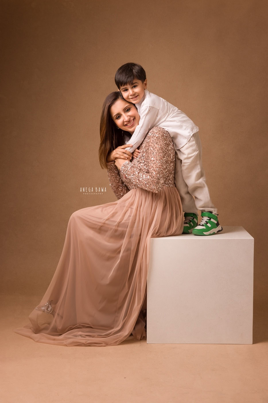 Elegant mother and son portrait, professional studio photography, warm beige background, deep emotional connection, high-quality family photo, Anega Bawa Photography.