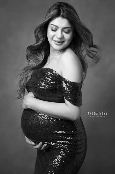 Black and white portrait of smiling expecting mother in an off-shoulder fitted sequin gown, looking over her shoulder, long wavy hair