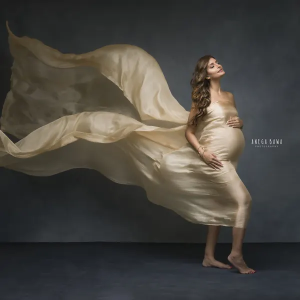 Expecting mother in a champagne gold silk drape with large sheer fabric sweeping out around her, barefoot, eyes closed and head back, hand
