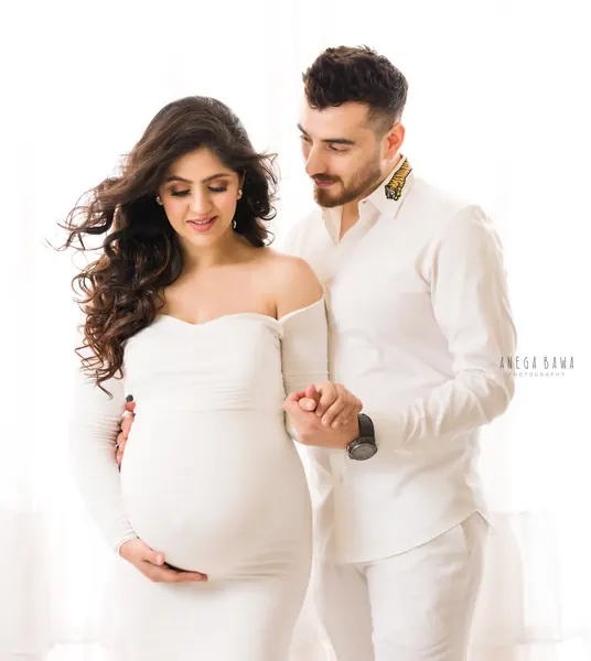 Couple in matching white outfits, wife in a white off-shoulder long-sleeve fitted dress with voluminous curls, husband in a white shirt