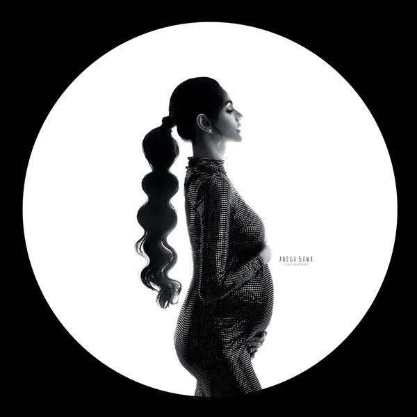 Black and white silhouette in a spotlight circle: expecting mother in profile with a long wavy ponytail in a fitted sequin high-neck gown