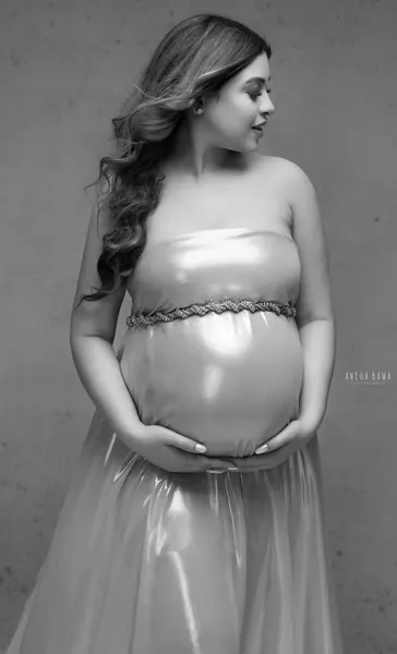 Black and white portrait of expecting mother in a strapless satin and tulle gown with a braided belt, looking to the side, hands under her