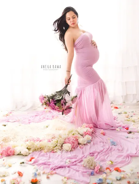 Expecting mother in a lilac strapless mermaid gown with a long train, holding a bouquet low in her hand with flowers and petals scattered
