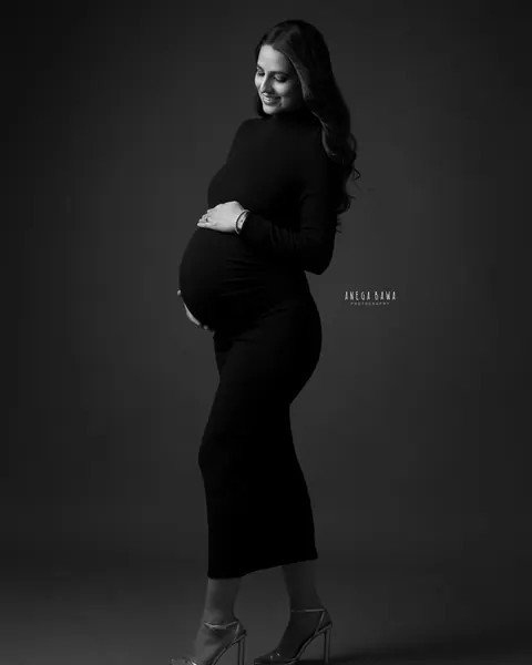 Maternity photography in Delhi: black and white full-length portrait of smiling expecting mother in a fitted black high-neck dress and