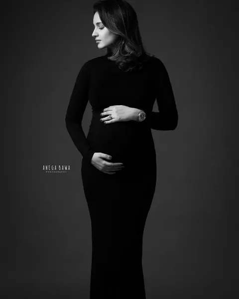 Maternity photography in Delhi: black and white full-length portrait of expecting mother in a fitted black high-neck gown looking to the