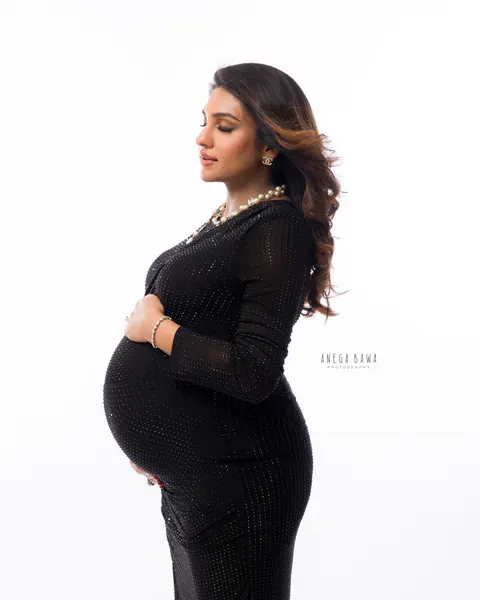 Maternity photography in Delhi: side profile of expecting mother with eyes closed in a black studded dress and layered pearl necklace