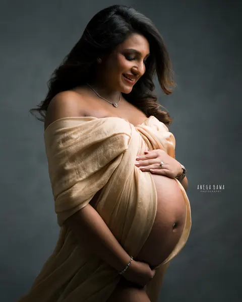 Maternity photography in Delhi: smiling expecting mother in a champagne silk drape off the shoulders, looking down and holding her bump
