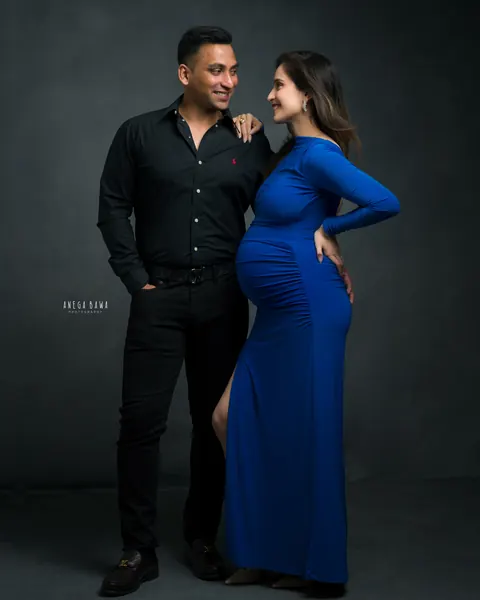 Maternity photography in Delhi: couple gazing at each other, wife in a royal blue gown with a hand on her back and husband in a black
