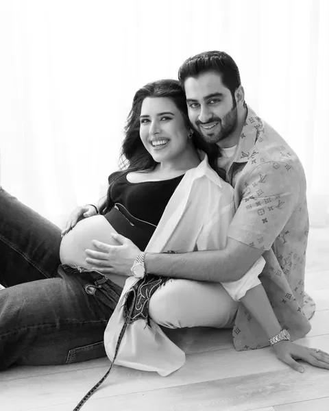 Maternity photography in Delhi: black and white portrait of a smiling couple seated on the studio floor, wife leaning back against her