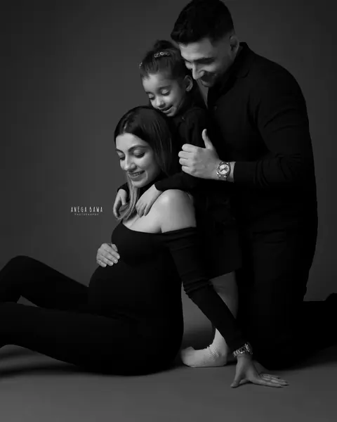 Maternity photography in Delhi: black and white family portrait, expecting mother seated on the floor with her daughter and husband leaning