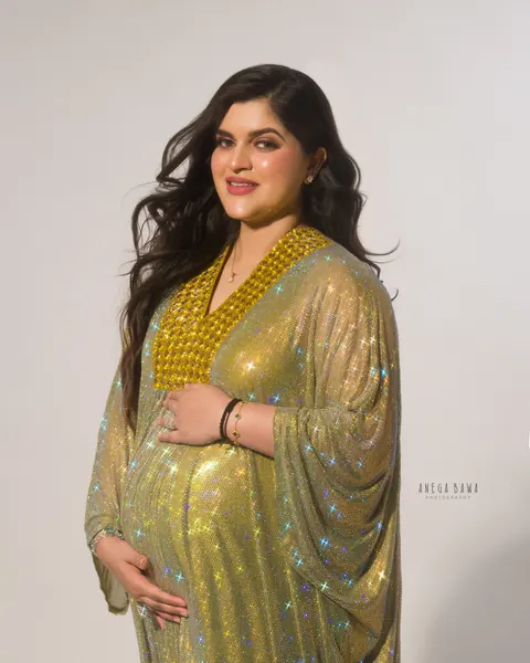 Maternity photography in Delhi: smiling expecting mother in a sparkling gold crystal kaftan gown with a jewelled neckline, hands on her