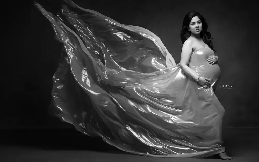 Maternity photography in Delhi: black and white portrait of expecting mother in a strapless metallic drape with the fabric billowing behind