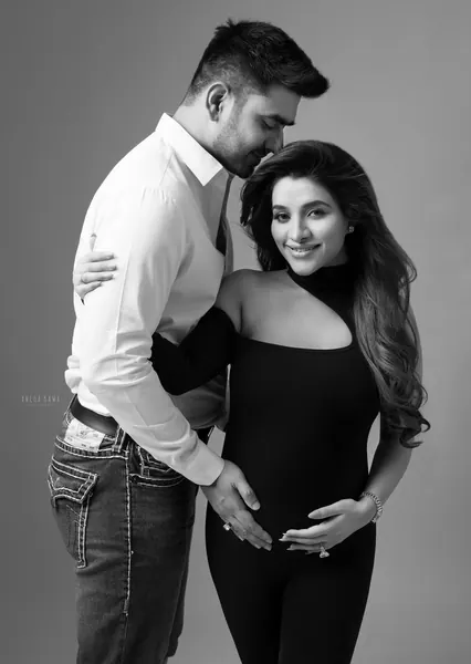 Black and white couple portrait: husband in a white shirt and jeans kissing his smiling wife's head and holding her bump, wife in a black