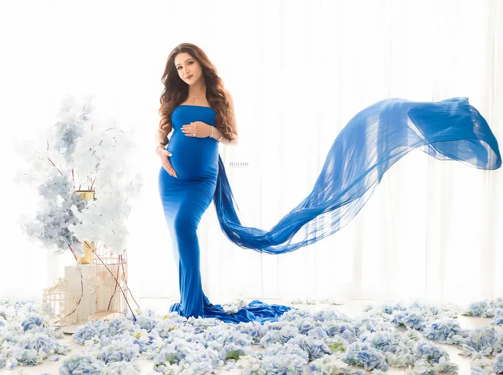 Expecting mother in a royal blue strapless fitted gown with a sheer blue train flying out to the side, surrounded by pale blue hydrangeas