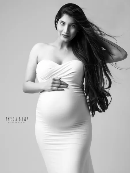 Black and white portrait of expecting mother in a white strapless sweetheart-neck fitted gown, long straight hair blowing, hand on her