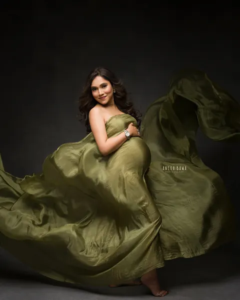 Maternity photography in Delhi: expecting mother twirling in an olive green satin drape with the fabric in motion, dark studio backdrop, by