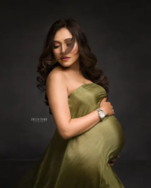 Maternity photography in Delhi: expecting mother in an olive green strapless drape with windswept hair across her face, hands on her bump