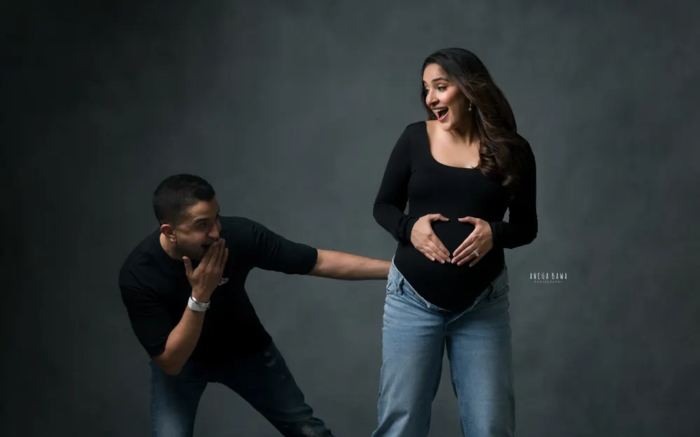 Maternity photography in Delhi: playful couple, wife making a heart shape with her hands on her bump while her husband reacts with a hand