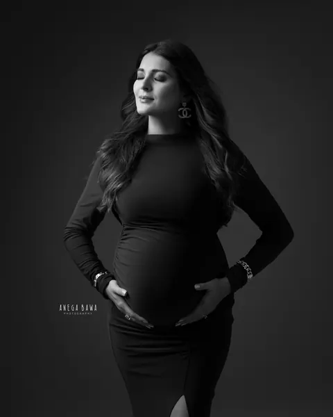 Maternity photography in Delhi: black and white portrait of expecting mother in a fitted ruched long-sleeve gown with eyes closed and hands