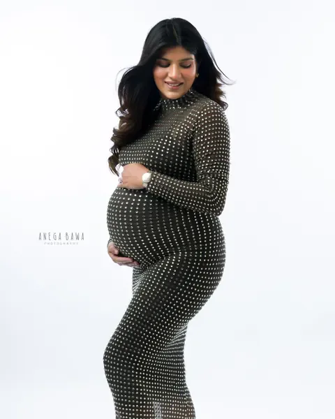 Maternity photography in Delhi: expecting mother in a fitted high-neck sheer gown covered in crystal studs with a side slit, looking down