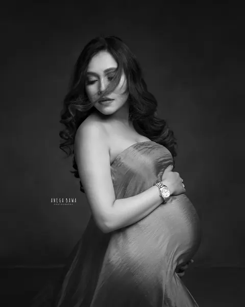 Maternity photography in Delhi: black and white portrait of expecting mother in a strapless drape with windswept hair across her face, by