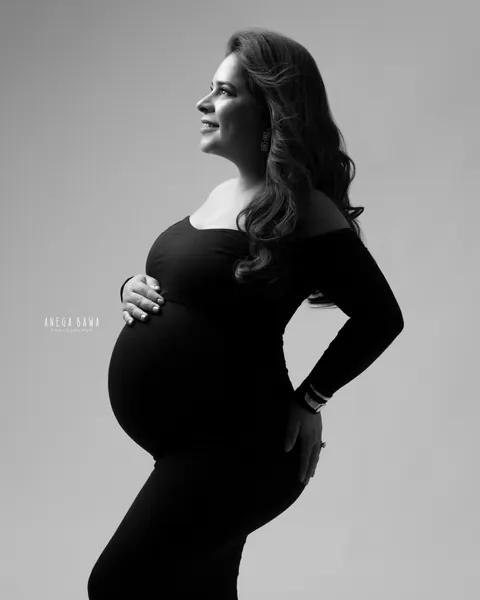 Maternity photography in Gurgaon: black and white profile of expecting mother in an off-shoulder black gown looking up with one hand on her