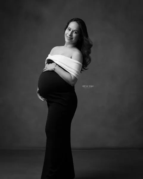 Maternity photography in Gurgaon: black and white portrait of smiling expecting mother in a black gown with a white off-shoulder wrap