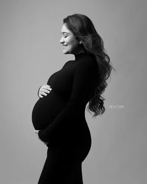 Maternity photography in Gurgaon: black and white side profile of smiling expecting mother in a fitted high-neck gown with long wavy hair