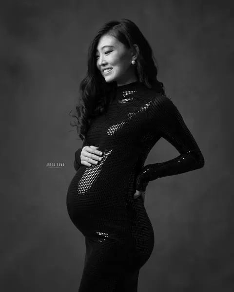 Maternity photography in Gurgaon: black and white side profile of smiling expecting mother in a high-neck sequin gown with a hand on her