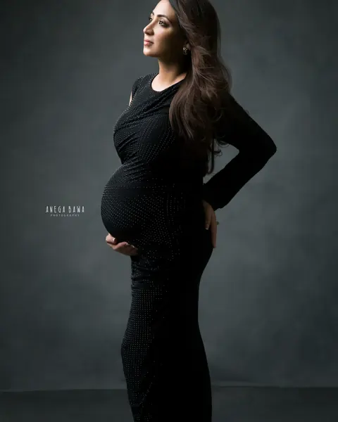 Maternity photography in Gurgaon: expecting mother in profile in a fitted black gown with a studded finish, hand on her back, looking up