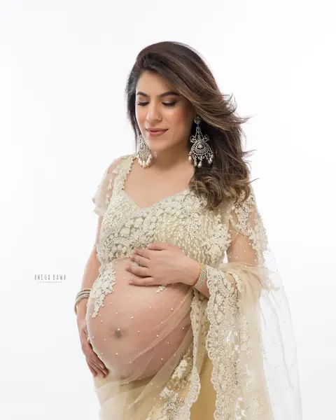 Maternity photography in Gurgaon: expecting mother in a champagne pearl-embroidered net saree and chandelier earrings, looking down at her