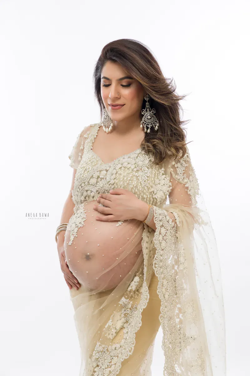 Maternity photography in Gurgaon: expecting mother in a champagne pearl-embroidered net saree and chandelier earrings, looking down at her