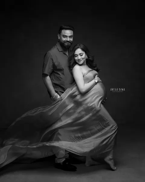 Maternity photography in Gurgaon: black and white portrait of a couple, wife in a flowing drape and husband standing behind with a hand in