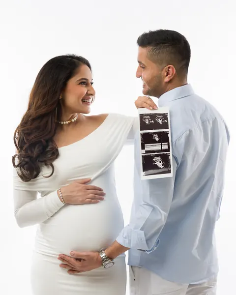 Maternity photography in Gurgaon: smiling couple looking at each other while the husband holds up ultrasound scan photos, wife in a fitted