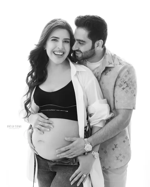 Maternity photography in Gurgaon: black and white portrait of a laughing couple, husband in a patterned shirt hugging his wife from behind