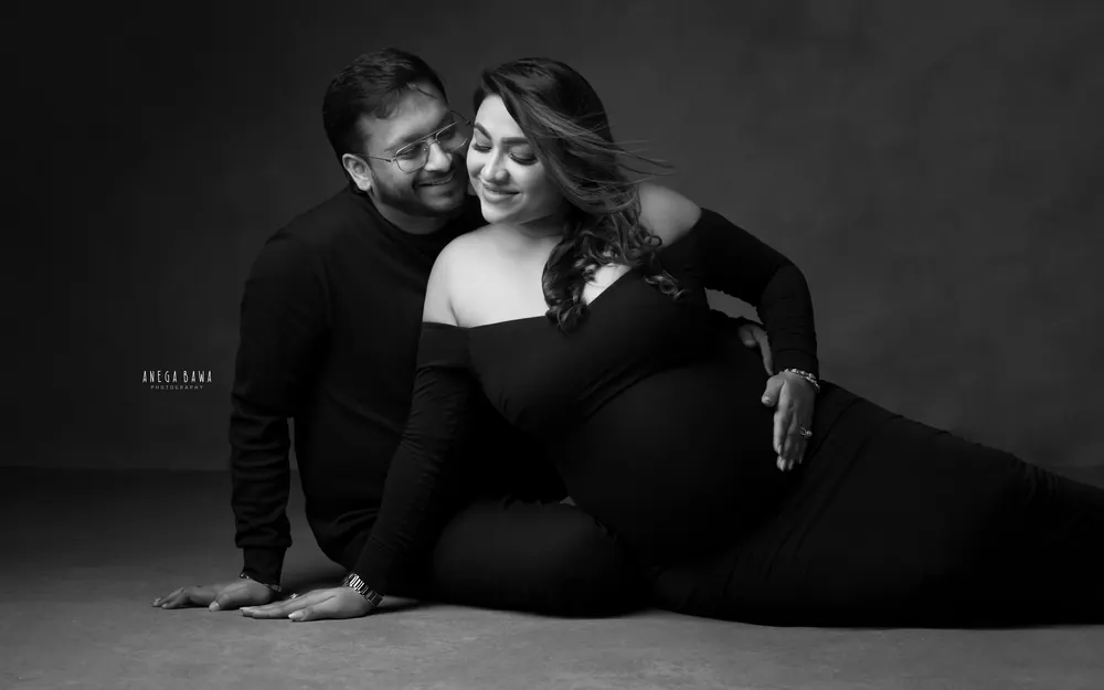 Maternity photography in Gurgaon: black and white portrait of a couple on the studio floor, wife reclining in an off-shoulder black gown