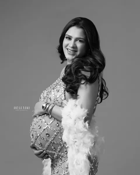 Maternity photography in Gurgaon: black and white portrait of smiling expecting mother in a crystal-embellished gown with a white feather