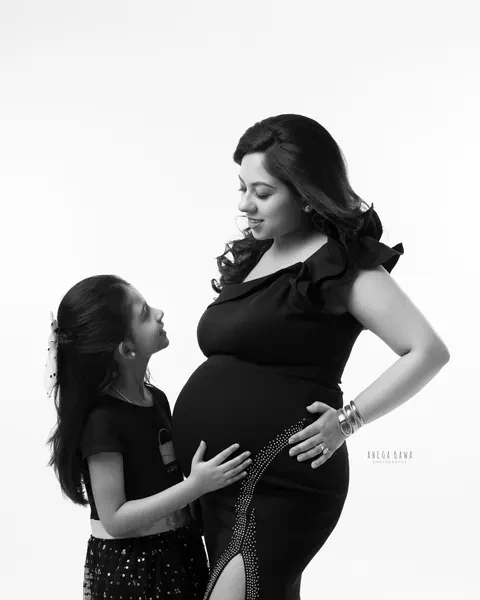 Maternity photography in Gurgaon: black and white portrait of a young daughter looking up at her expecting mother and touching her bump