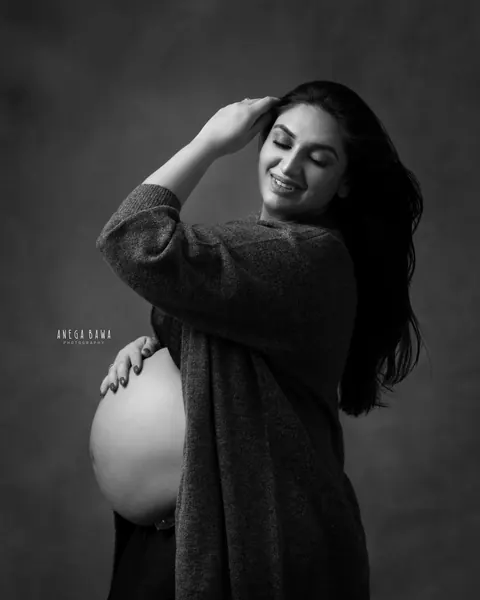 Maternity photography in Gurgaon: black and white portrait of smiling expecting mother in an open cardigan with one hand in her hair and