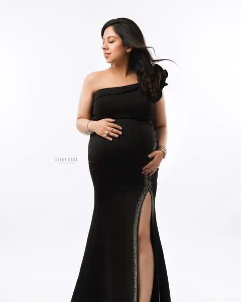 Maternity photography in Gurgaon: expecting mother in a full-length black one-shoulder gown with a crystal-trimmed high slit and gold