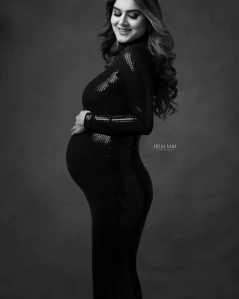 Maternity photography in Gurgaon: black and white side profile of expecting mother in a fitted high-neck sequin gown, smiling down at her